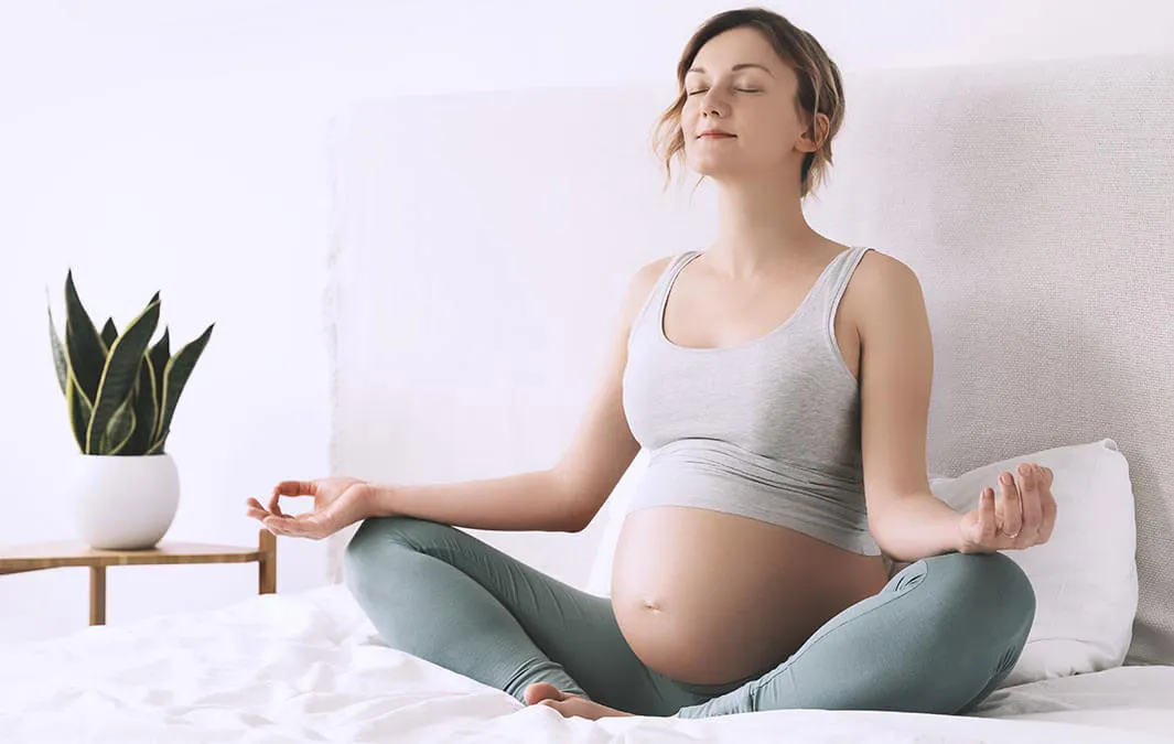 Nosečnica sproščeno meditira na postelji